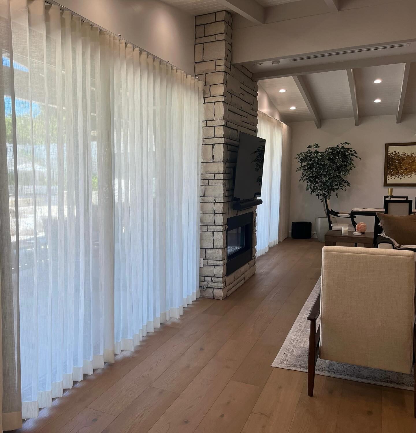 Sheer drapery running a full living room wall beside a stone fireplace in San Diego