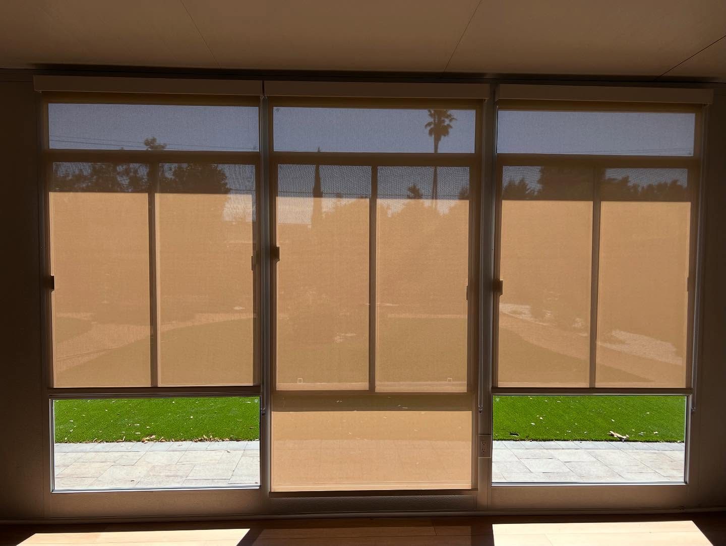 Bronze solar shades lowered over three sliding glass doors in a San Diego home, the garden still clearly visible through the screen fabric