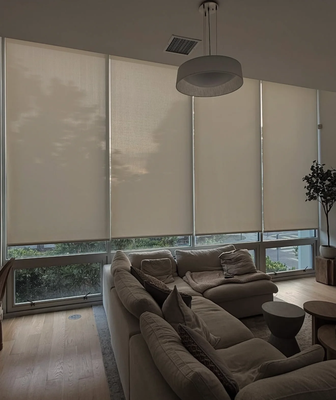 Roller shades lowered across a wall of windows in a living room with a sectional sofa