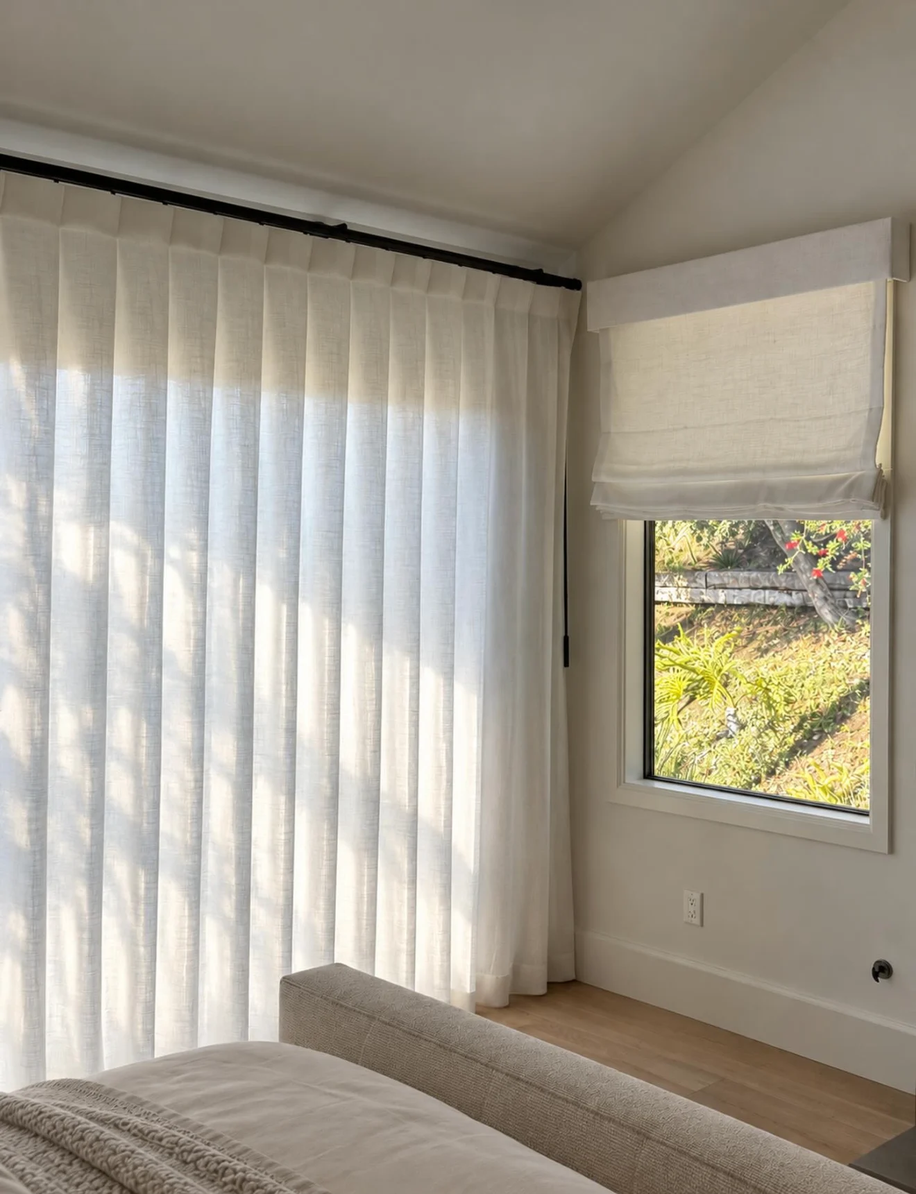 A Roman shade beside sheer drapery on a bedroom window