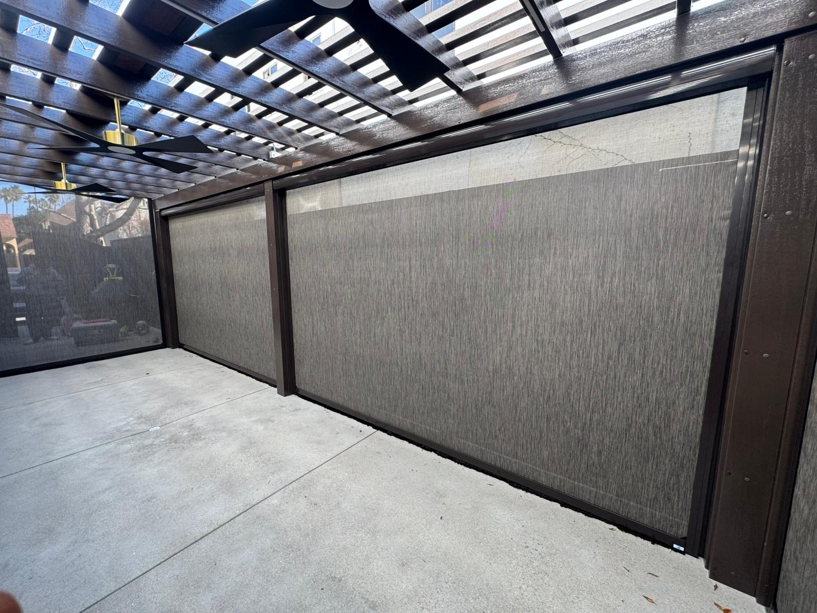 Two zip screens lowered across a pergola patio, running in bronze side tracks